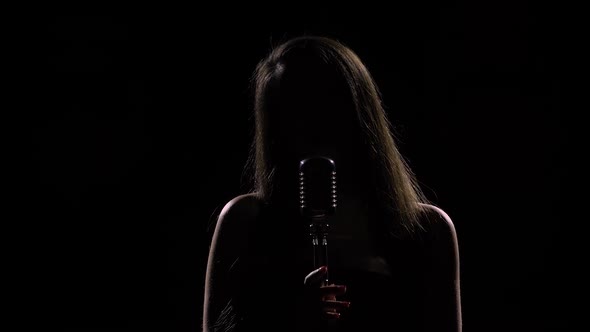 Silhouette of Young Woman Singing Into Retro Microphone