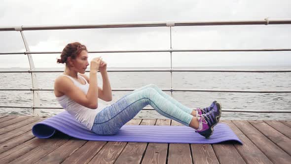Closeup View of Young Athletic Woman Doing Situps on the Mat By the Ocean in the Early Morning