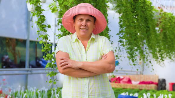 Front View of a Senior Florist Woman in a Greenhouse Female Crosses Arms and Smiles Playfully