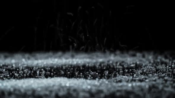 White Granulated Sugar Pours Onto a Black Glass Surface Creating a Slide