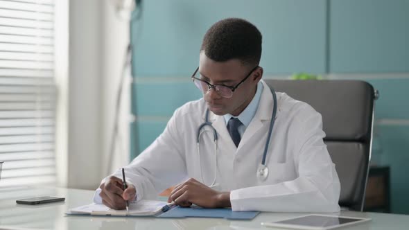 Young African Doctor Writing on Paper in Clinic