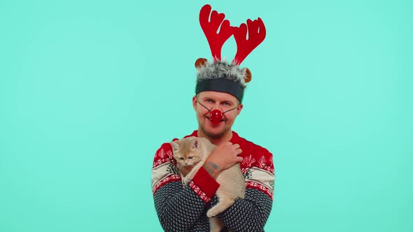 Lovely Adult Man in Fashionable Christmas Sweater and Deer Antlers Hat Holding His Beloved Cat Pet