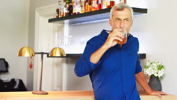 Portrait of smiling mature man drinking wine while standing at counter