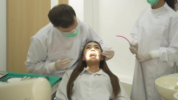 A dentist checking up Asian woman patient's teeth by using dental mouth mirror at hospital