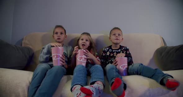 Group of Children Watching Movie on TV in the Evening at Home and Eat Popcorn