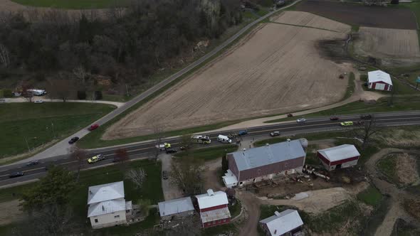 View over rural highway with rescue vehicles at the scene of an accident in front of farm with rain