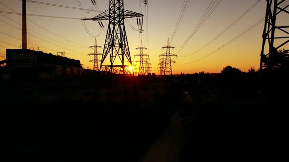 Power station near the river at sunset. Tall silhouettes of high-voltage electric lines