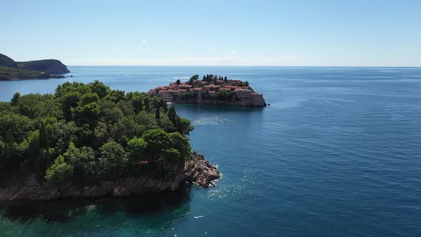 Drone flying over trees and sea, focusing on Sveti Stefan peninsula. Sunny, summer day over tourist