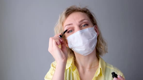 Curly Blonde Joyful Girl in Medical Protective Mask Paints Eyelashes Does Makeup