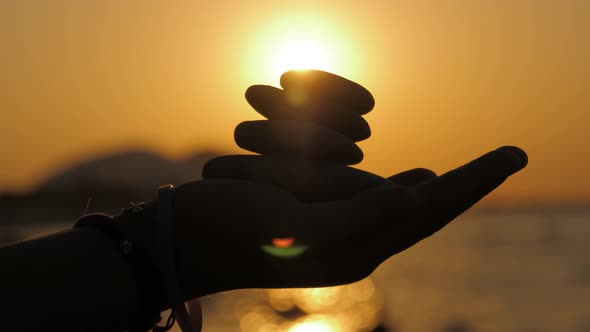 Silhouette of a Hand with Pebble Stones on a Background of Sunset and Sea. Balance Concept.