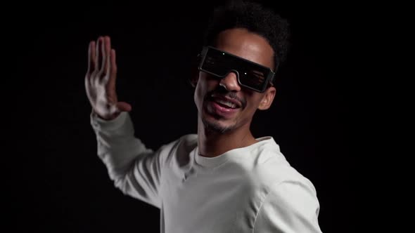 African Man in Glowing Neon Glasses Moving to Music Rhythm on Black Studio Background. 