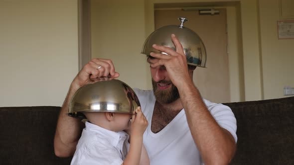 A Father is Playing with His Son with the Lids From the Dishes in the Hotel