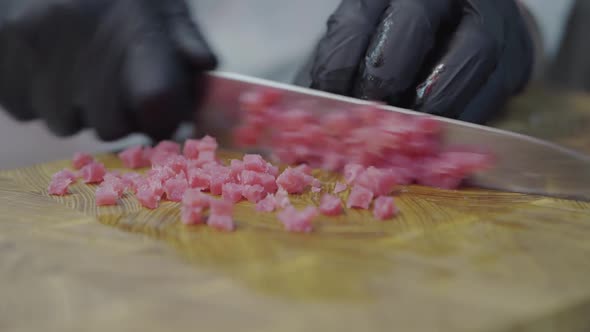 Hands of Chef in Restaurant Uniform and Black Gloves Cutting Slices of Tuna Fish