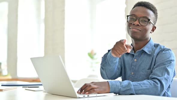 Young African Man with Laptop Pointing with Finger at Camera