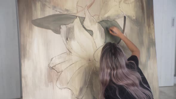 Back view of young female artist painting flowers on canvas