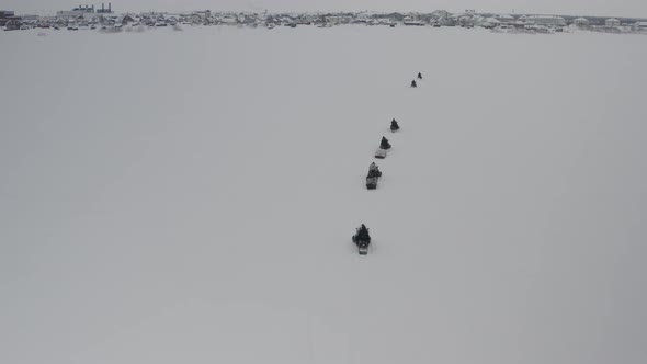 A Group of Travelers Ride Along the Frozen River on Snowmobiles