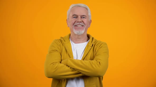 Smiling Elderly Man With Folded Arms Winking at Camera