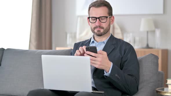Young Businessman Using Smartphone and Laptop at Home