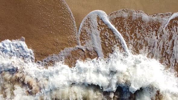 Top view of the sandy shore washed by the waves of the sea, foamy water boiling with waves.