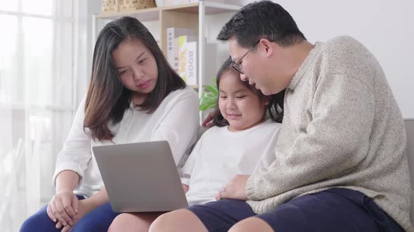 Happy young family with a kid sit on sofa in living room have fun using modern laptop together