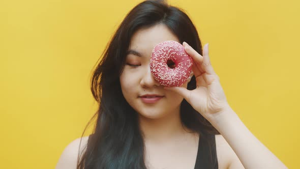 Attractive Asian Woman Having Fun Putting Donuts Over the Eyes