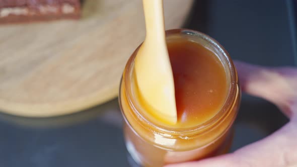 Closeup White Spoon Stirs a Full Jar of Liquid Homemade Salted Caramel