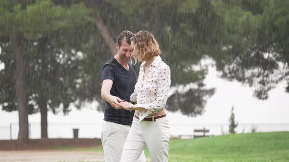 A Romantic Couple Dancing and Lovingly Playing in the Pouring Rain at a Park, Slow Motion