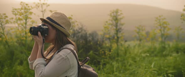 A Young Girl with Backpack and a Hat Taking Pictures of Landscape at Sunset