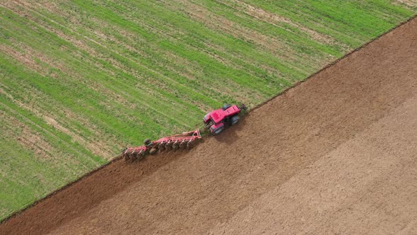 Red Tractor Ploughs A Green Agricultural Field To Increase Harvest Aerial View