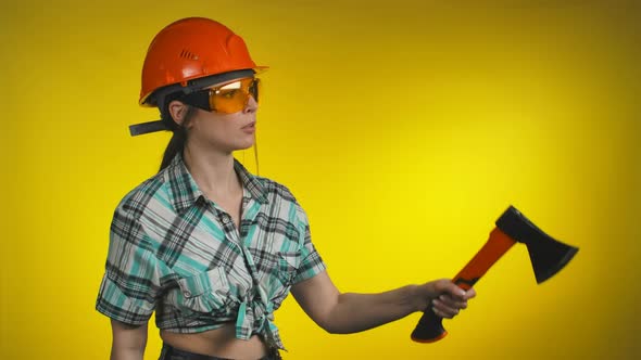 A Female Builder in an Orange Safety Helmet Holds an Ax in Her Hands