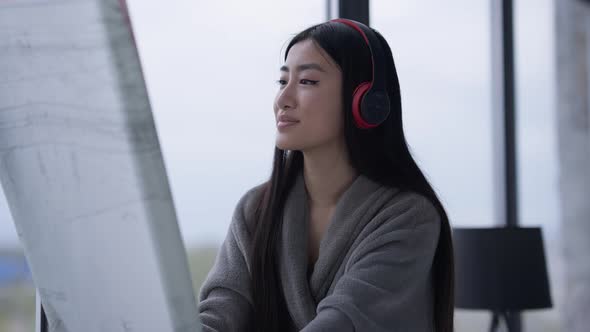 Young Creative Female Architect Looking Through Blueprint Sitting on Windowsill in Home Office