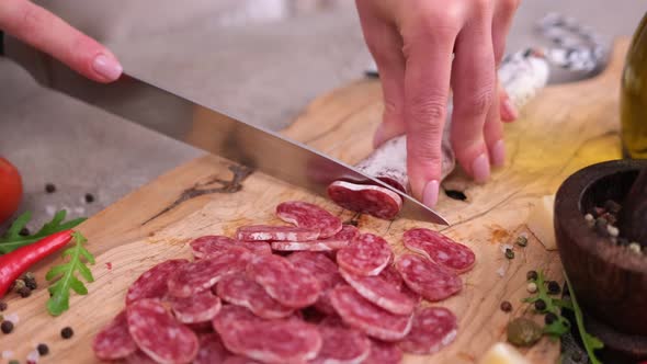 Woman Slicing Fuet Sausage with Knife at Domestic Kitchen