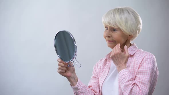 Elderly Woman Looking at Wrinkled Face in Mirror, Thinking About Plastic Surgery