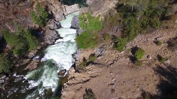 Kayakers carrying their colorful kayaks along the shore to avoid a dangerous waterfall in a rugged c