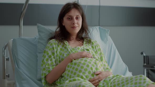 Portrait of Adult with Pregnancy Holding Belly in Hospital Ward