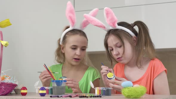 Two Girls with Bunny Ears Decorate Easter Eggs Together and Talk