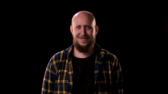 Bald Bearded Man in Checkered Shirt Looks Intently and Angrily at the Camera on Black Background