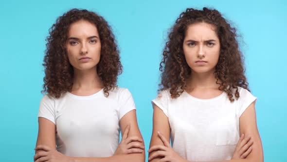 Two Grumpy Resentful Young Caucasian Female Twins in White Tshirts Standing Close to Each Other with