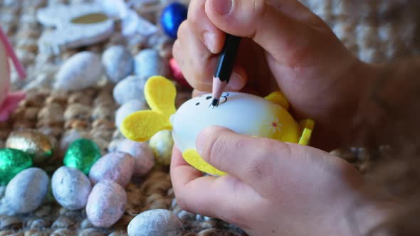 A girl draws a pattern on an Easter egg in the form of a rabbit with Easter eggs in the background