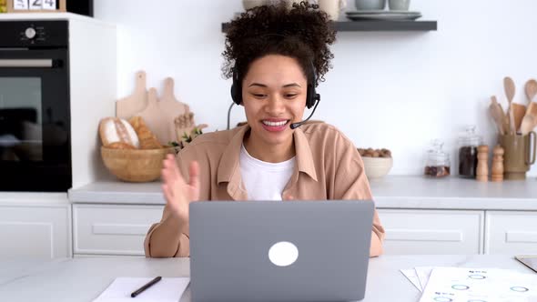 Positive African American Girl with Headset Freelancer Advisor Student Sits at Desk in the Kitchen