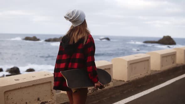 Rare View of Sporty Builded Woman in Hat Coat and White Sneakers Enjoying Time By the Seaside on a