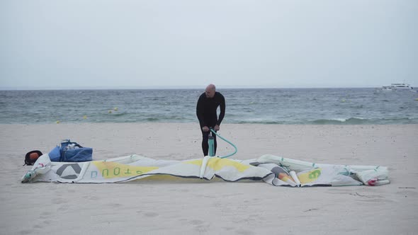 Man Pumping an Inflatable Kite on the Sand Beach