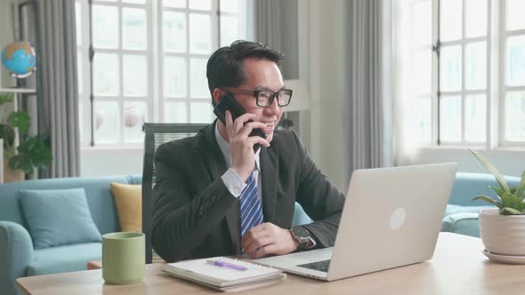 Asian Businessman Answering The Phone Call While Using Working At Home