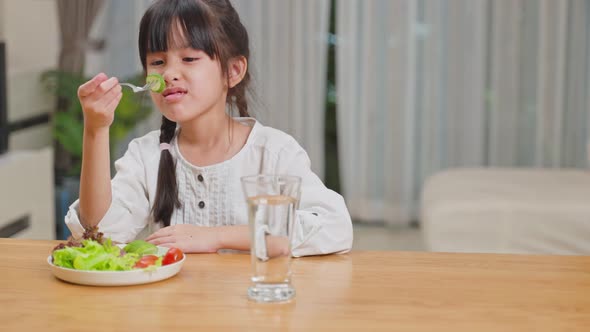 Unhappy Asian little young girl child don't want to eat green vegetables on dinner plate at home.