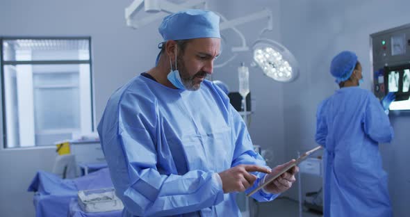 Portrait of caucasian male surgeon standing in operating theatre using tablet