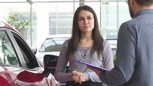 Young Woman Talking to the Salesman at the Car Dealership