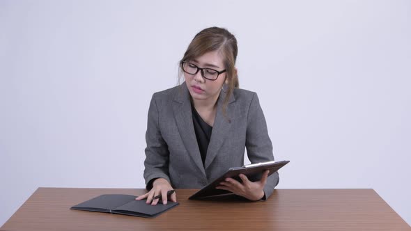 Young Happy Asian Businesswoman Reading on Clipboard and Book at Desk