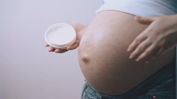 Pregnant Lady Applies Cream on Belly at White Wall Closeup
