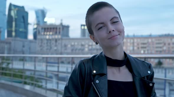 Young Attractive Stylish Woman with Short Shaved Hair Against Urban Background with Skyscrapers at