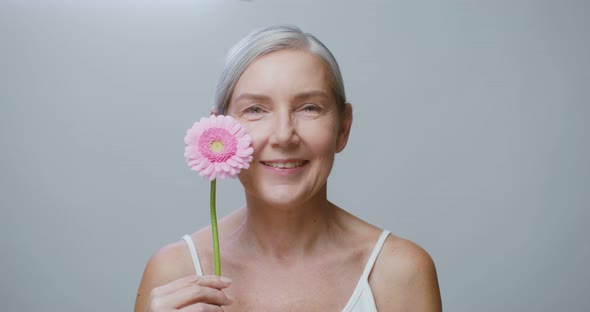 An Aged Caucasian Model Posing with a Gerbera Flower Stroking Her Face